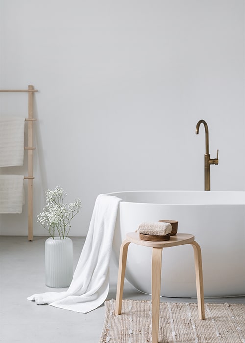 A clean white bath, accompanied by a rustic wooden stool, enhancing the bathroom's aesthetic appeal.